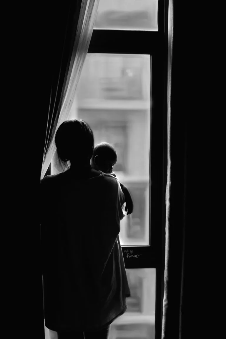 Silhouette of a mother holding her baby at a tall window