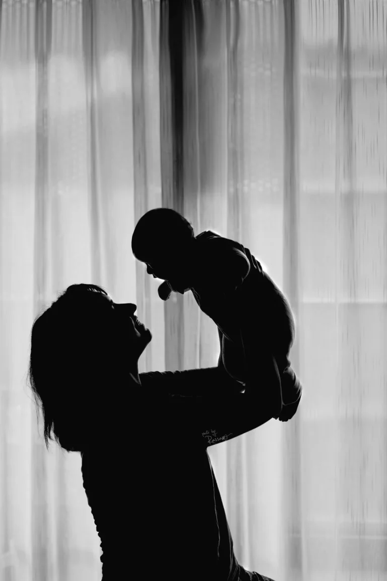 Silhouette of a mother lifting her baby against sheer curtains