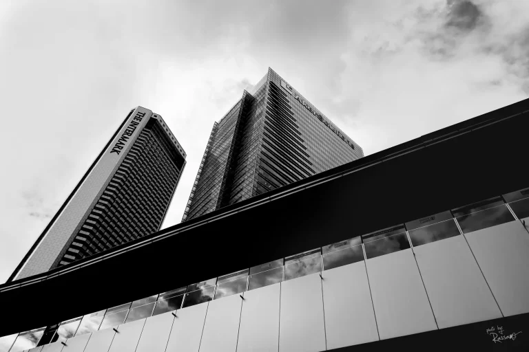 Twin office towers rising above a glass walkway, black and white