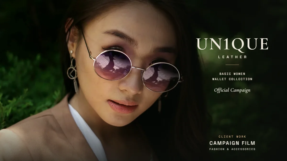 UN1QUE Leather campaign poster: a woman in round rose-tinted sunglasses against green foliage