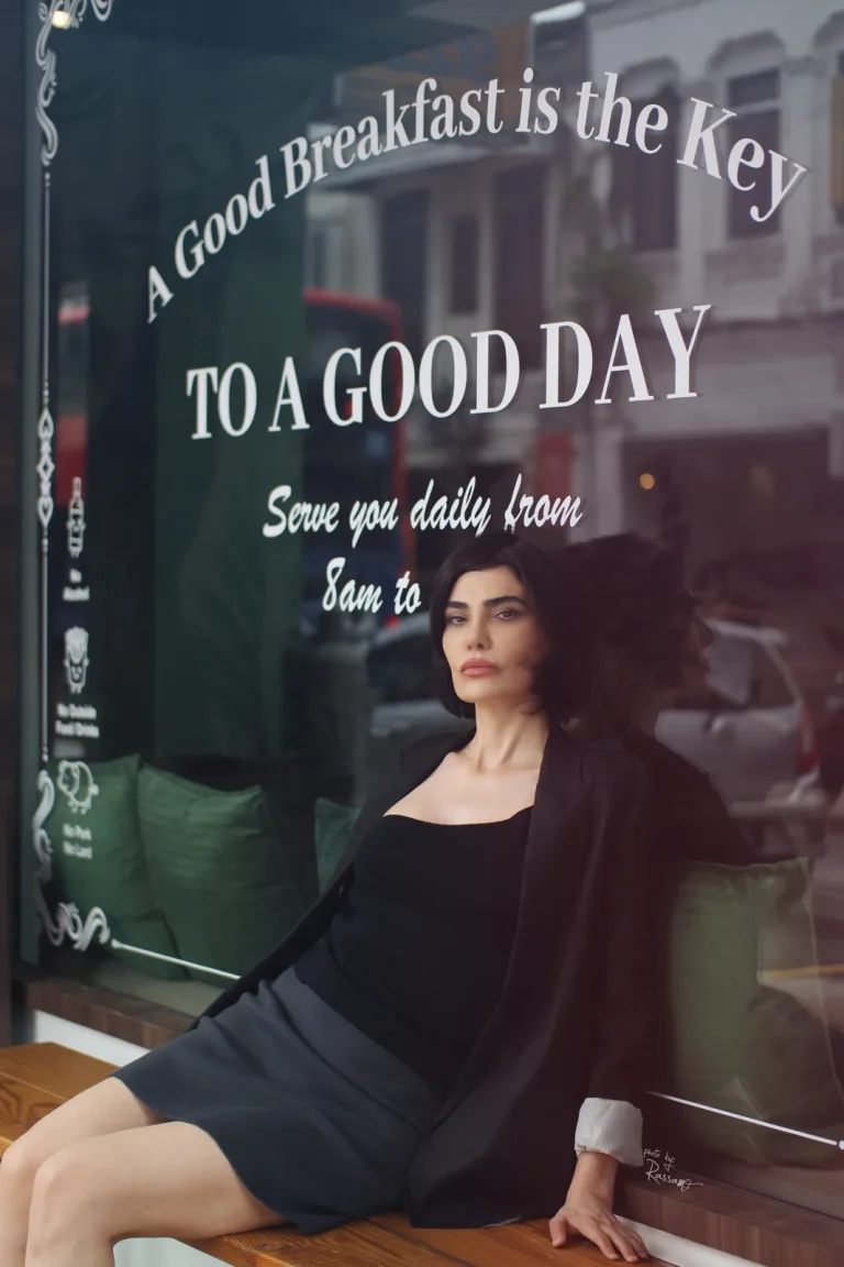 Woman in a black blazer sits on a ledge against a cafe window lettered 'A Good Breakfast is the Key'.