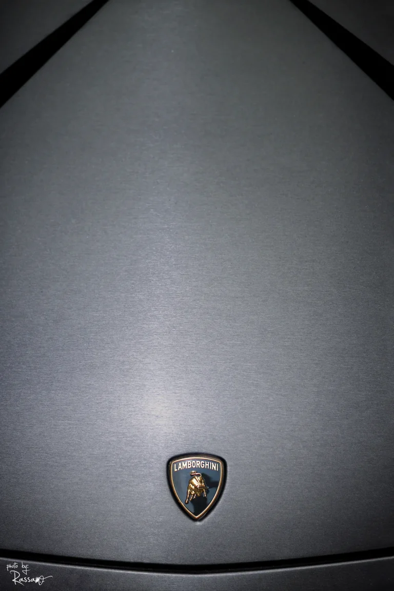 Minimal view of a brushed grey Lamborghini bonnet with the gold bull badge near the bottom edge.