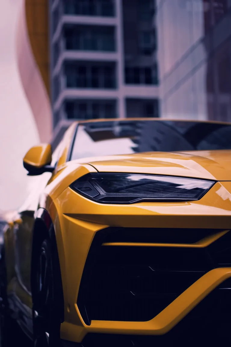 Yellow Lamborghini Urus front corner and headlight against blurred city towers, cinematic grade.