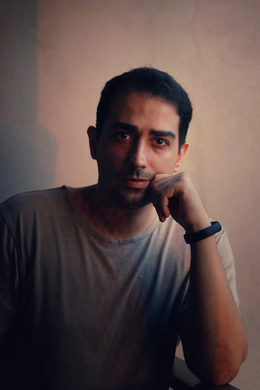 Rassam Feali, filmmaker and photographer, seated with his chin resting on his hand