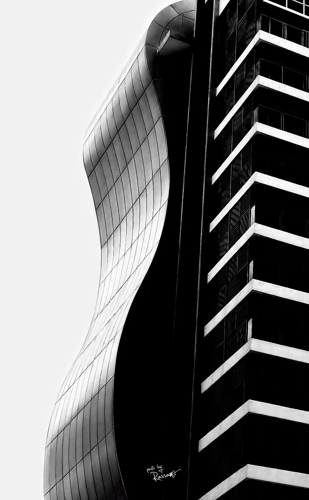 Reality & Truth I: a curved glass facade beside a striped tower, seen from below, black and white