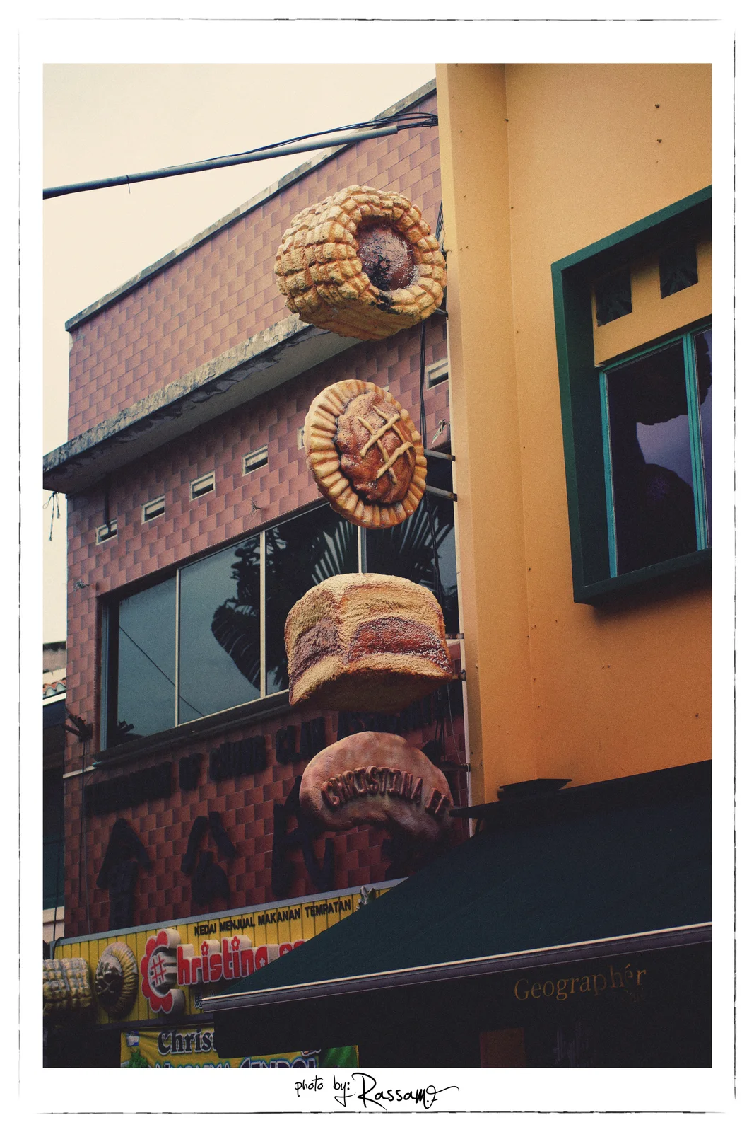 A bakery sign made of giant bread and pastries mounted on a pink tiled shop front