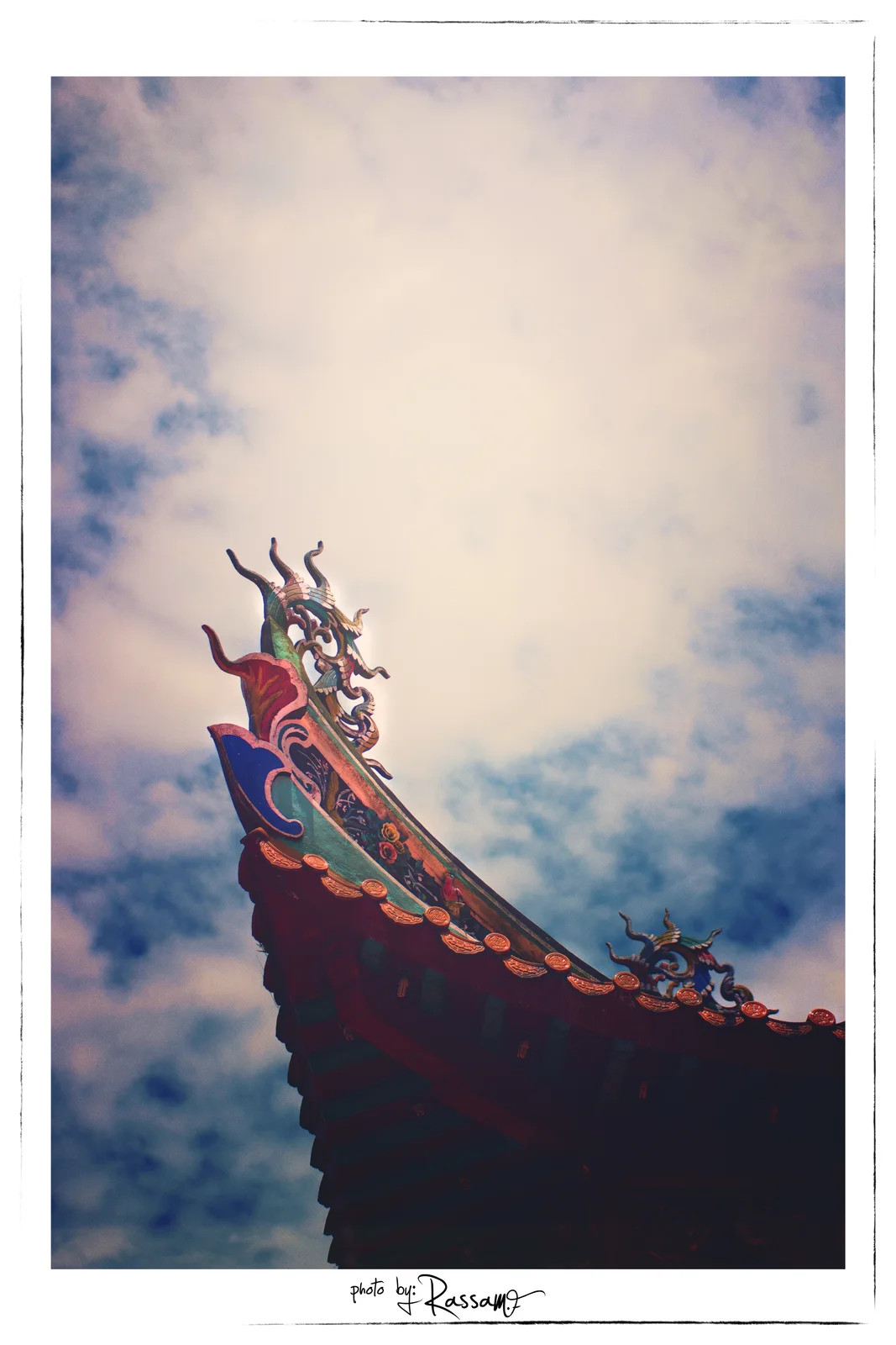 The curled tip of a temple roof ending in a small dragon, almost the whole frame filled with bright sky