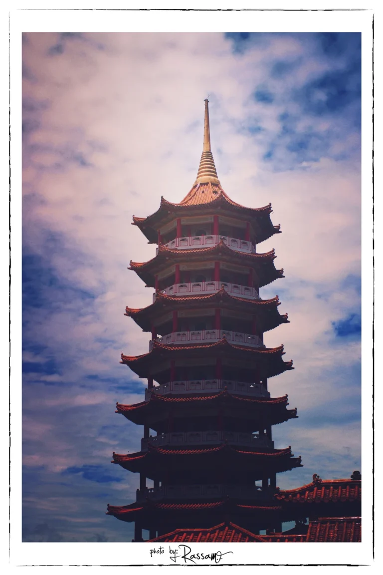 A tall red pagoda with a golden spire against blue sky and clouds
