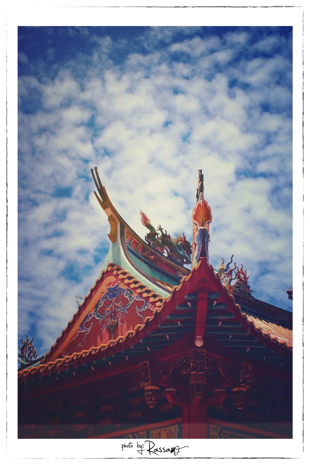 A red and gold painted temple gable with dragons on the ridge against a blue cloudy sky