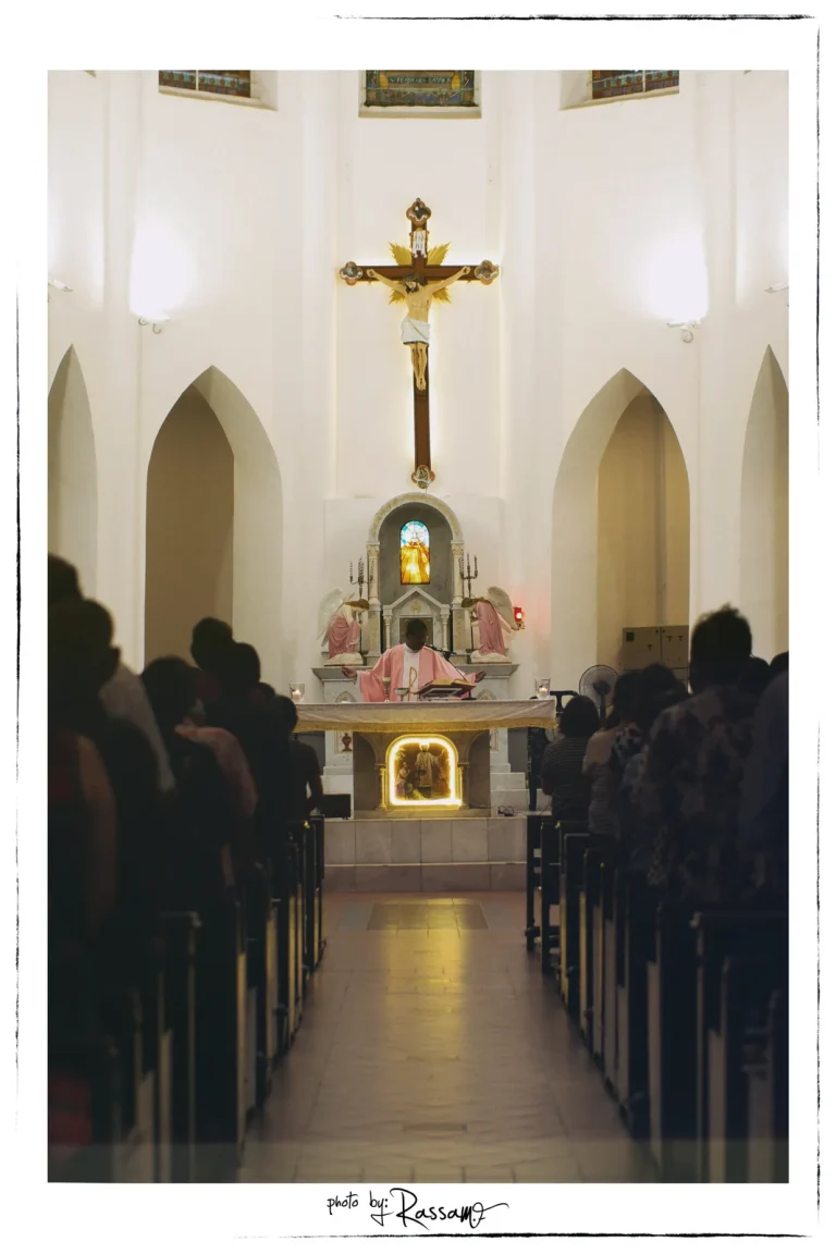 The aisle of St. Francis Xavier's Church during a service, people in silhouette and a lit altar